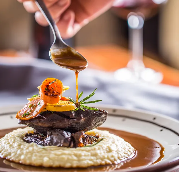 Un chef verse de la sauce sur un plat de viande élégamment présenté avec des légumes à Chénérailles dans la Creuse 23