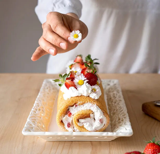 Main décorant un gâteau roulé fraise et crème avec une pâquerette à Chénérailles dans la Creuse 23