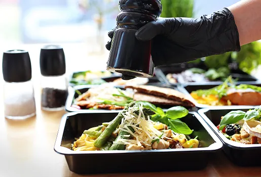 Main gantée noire moulant du poivre sur des repas préparés en barquettes à Chénérailles dans la Creuse 23