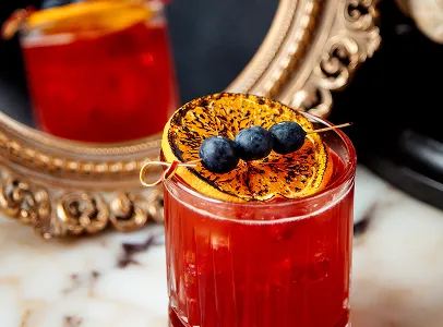 Cocktail rouge avec orange grillée et myrtilles, reflété dans un miroir doré à Chénérailles dans la Creuse 23