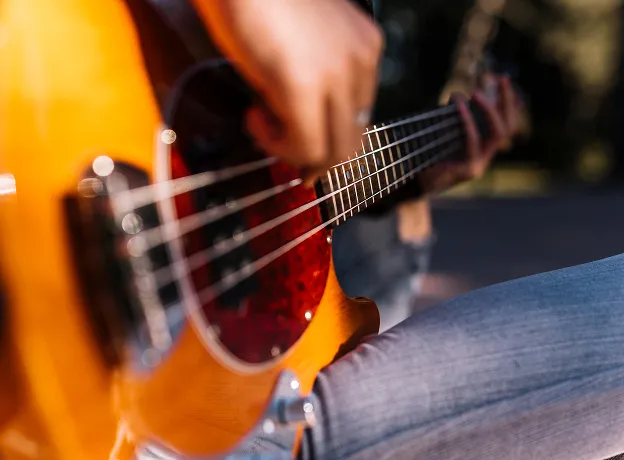 Gros plan d'une personne jouant de la guitare basse électrique orange et rouge.